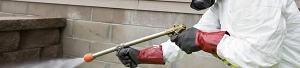 Pest control technician applying exterior insect treatment along a home foundation in Chandler, AZ