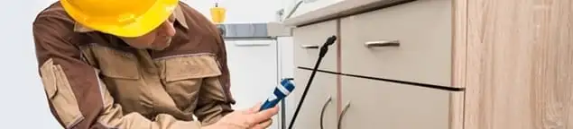 Roach exterminator applying treatment under kitchen cabinets in Chandler, AZ