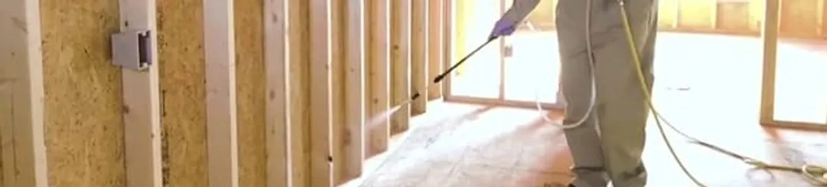 Termite treatment technician applying spray along framing and unfinished walls in Chandler, AZ