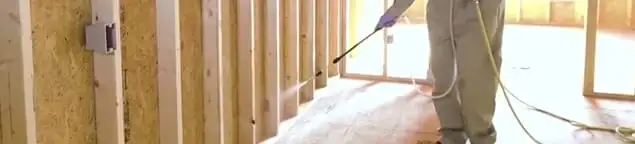 Termite treatment technician applying spray along framing and unfinished walls in Chandler, AZ